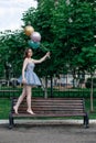 a happy young woman in a blue short corset dress walks barefoot on a bench and holds flying balloons, a romantic girl on Royalty Free Stock Photo