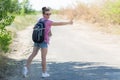 Happy young woman with bundled hair and tourist backpack hitchhiking on the road. Copyspace Royalty Free Stock Photo