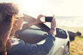 Happy young woman in car with smartphone at sea Royalty Free Stock Photo