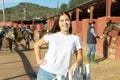 Happy young woman in casual clothes standing near fence and smiling at camera during visit of horse ranch Royalty Free Stock Photo