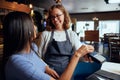 Happy young woman in casual clothing paying for dinner with card machine by waitress Royalty Free Stock Photo