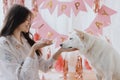 Happy young woman celebrating dog first birthday with donut and candle in room with pink decorations Royalty Free Stock Photo