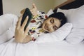 Happy young woman checking on her phone while lying in bed Royalty Free Stock Photo