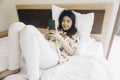 Happy young woman checking on her phone while lying in bed Royalty Free Stock Photo