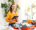 Happy young woman checks a list of things with a tablet, collects a suitcase, getting ready for the trip, vacation, travel