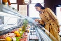 Happy young woman choosing meat from glass cabinet in grocery store Royalty Free Stock Photo