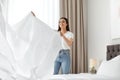 Happy young woman with clean bedsheet in room