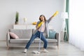 Happy young woman cleaning her home, singing at mop like at microphone and having fun, free space Royalty Free Stock Photo