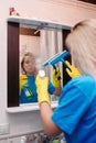 Woman cleaning with spray and using squeegee to wash mirror at bathroom. Royalty Free Stock Photo