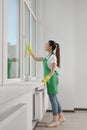 Happy young woman cleaning window glass with rag indoors Royalty Free Stock Photo