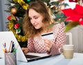 Happy young woman with credit card and laptop sitting at home against background of Christmas tree Royalty Free Stock Photo