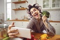 Happy young woman in curlers taking funny selfie with broccoli head in the kitchen Royalty Free Stock Photo