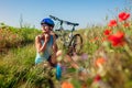 Happy young woman cyclist taking her helmet off after riding bicycle in summer poppy field. Having rest after workout