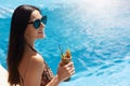 Happy young woman in dark sunglasses holding cocktail while standing next to swimming pool. Female in bikini with leopard print Royalty Free Stock Photo