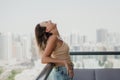 Happy young woman in denim shorts and beige crop top standing at the balcony. Positive attitude