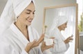 Happy young woman applying face cream while doing her skin care routine in the bathroom Royalty Free Stock Photo