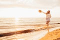 Happy young woman in a dress holding straw hat and walking alone on empty sand beach at sunset sea shore and smiling. Freedoom, Royalty Free Stock Photo