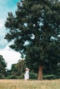 A happy young woman in a dress and a straw hat runs across the field. In the background is a large tree and a stormy sky Royalty Free Stock Photo