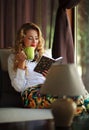 Happy young woman drinking coffee and reading book on couch Royalty Free Stock Photo