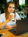 Happy young woman drinking coffee/tea and using laptop in a cof Royalty Free Stock Photo