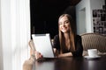 Happy young woman drinking coffee or tea and using tablet computer in a coffee shop Royalty Free Stock Photo