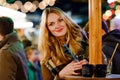 Happy young woman drinking hot punch, mulled wine on German Christmas market. Happy person in winter clothes with lights