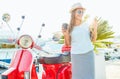 Happy young woman drinking takeaway coffee near her red moped in Royalty Free Stock Photo