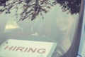 Happy young woman driver inside her car with hiring sign on windshield