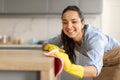 Happy young woman dusting off wooden table at kitchen Royalty Free Stock Photo