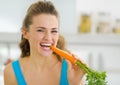 Happy young woman eating carrot in kitchen Royalty Free Stock Photo