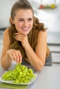 Happy young woman eating grape in kitchen Royalty Free Stock Photo