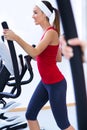 Happy young woman with elliptic machine in the gym