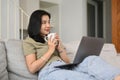 Happy young woman enjoy her morning coffee and using laptop on couch at home Royalty Free Stock Photo