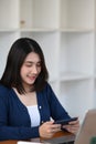 A young woman enjoy playing game application on mobile phone while sitting in front of her computer laptop. Royalty Free Stock Photo