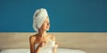 Happy young woman enjoying with cup of coffee drying her wet hair after bath with wrapped towel on her head sitting on bed looking Royalty Free Stock Photo