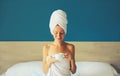 Happy young woman enjoying with cup of coffee drying her wet hair after bath with wrapped towel on her head sitting on bed in the Royalty Free Stock Photo