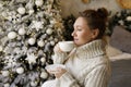 Happy young woman enjoying drinking tea or coffee in living room with Christmas decor Royalty Free Stock Photo