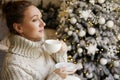 Happy young woman enjoying drinking tea or coffee in living room with Christmas decor Royalty Free Stock Photo
