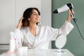 Happy young woman enjoying hair drying routine, home interior Royalty Free Stock Photo