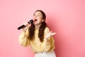 Happy young woman enjoying playing karaoke, singing in mic, looking aside at screen with lyrics, smiling cheerful