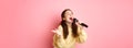 Happy young woman enjoying playing karaoke, singing in mic, looking aside at screen with lyrics, smiling cheerful