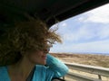 Happy young woman enjoying trip while traveling in car. Woman in sunglasses looking outside window. Woman with tousled hair Royalty Free Stock Photo