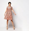 Happy woman with evening hair style dancing in a short flying pink sequined dress and glossy high heel shoes, on white