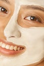 Happy young woman with facial mask applied on half of her face receiving spa treatments, smiling at camera