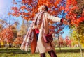 Happy young woman feeling free and happy walking in autumn park among red trees. Female fall fashion Royalty Free Stock Photo