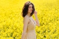 Happy young woman in field with yellow flowers on sunny summer day, closeup portrait. Pretty caucasian model girl with curly hair Royalty Free Stock Photo
