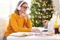 Happy young woman freelancer in headphones working remote at laptop at home before Christmas