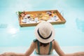 Happy young woman in green swimsuit having Floating Breakfast tray in luxury pool hotel, girl with hat enjoy in tropical resort. Royalty Free Stock Photo