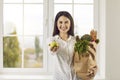 Happy young woman with a grocery bag smiling and holding out a fresh green apple Royalty Free Stock Photo