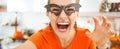 Happy young woman in Halloween decorated kitchen taking selfie